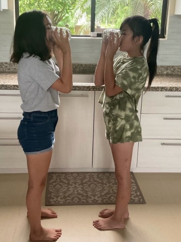 Alba and Rielle at age 10 drinking water in the kitchen
