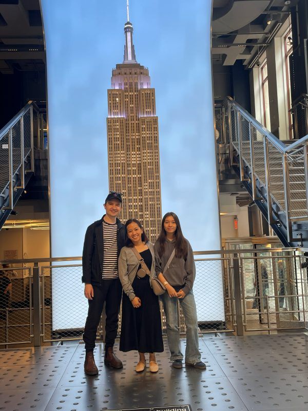Sean, Cher, and Alba posing in front of mural of Empire State Building in of the building